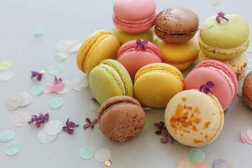 colorful macarons on trendy pastel gray paper with lilac flowers and confetti. tasty pink, yellow, green and brown macaroons. candy bar for party. food photography. yummy background