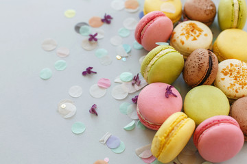 colorful macarons on trendy pastel gray paper with lilac flowers and confetti. tasty pink, yellow, green and brown macaroons. candy bar for party. food photography. yummy background