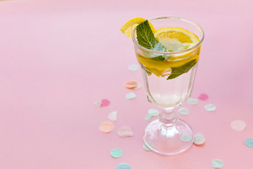 cocktail drink on trendy pink paper background with confetti. fresh mojito, water with lemon and mint. space for text. summer holidays. vacation and party concept