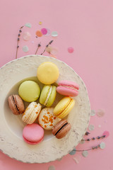 food photography flat lay of tasty colorful macarons in vintage plate on trendy pastel pink paper with lavender and confetti. space for text pink, yellow, green, white, brown macaroons.