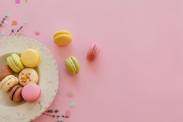 food photography flat lay of tasty colorful macarons in vintage plate on trendy pastel pink paper with lavender and confetti. space for text pink, yellow, green, white, brown macaroons.