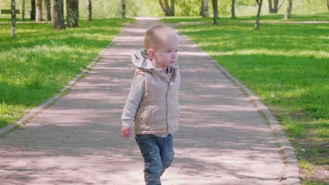 Little blond boy walks on path in park
