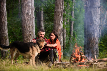 Couple pat german shepherd dog near bonfire, nature background.