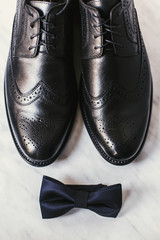 stylish black shoes and navy bow tie on marble background, top view. groom morning wedding preparations