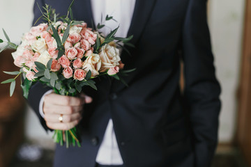 groom holding stylish bouquet with roses and eucalyptus. morning preparations before wedding day. groom waiting for his bride