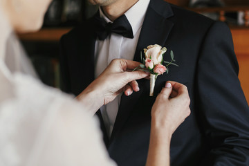 beautiful bride putting on stylish simple boutonniere with roses on groom black suit. wedding morning preparations - obrazy, fototapety, plakaty