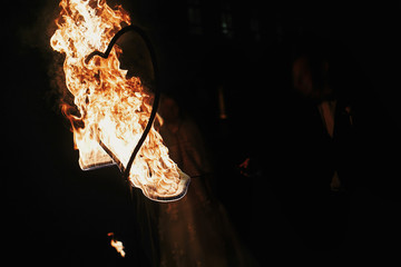 bride and groom holding burning hearts, amazing fire show at night at festival or wedding party....