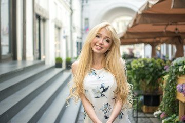 Beautiful young woman with perfect blonde hair wearing dress looking at camera and posing in the city street.