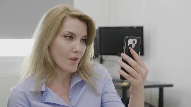 Jaw dropped office woman surfing on social media network using smartphone staring in shock at screen watching something disturbing
