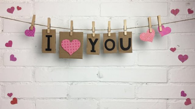 Frase &ldquo;I love you&rdquo; colgando de una cuerda con pinzas sobre fondo blanco con corazones.