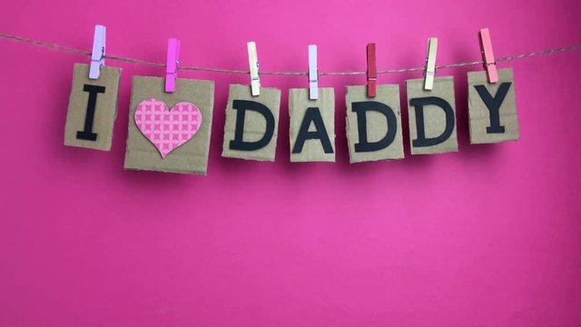 Frase &ldquo;I love dady&rdquo; colgando de una cuerda con pinzas sobre fondo rosa.