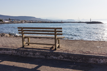 Fototapeta na wymiar wooden bench on sunny at sea view, in front of beautiful with mountains and boats