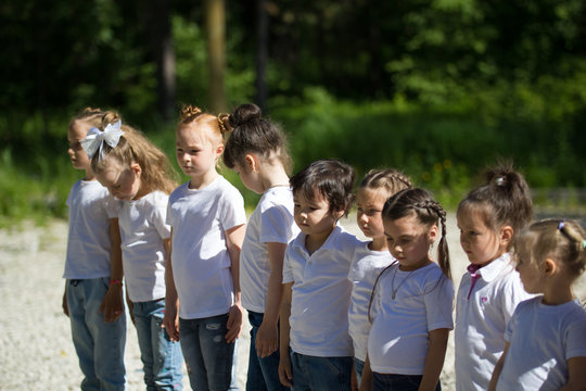 Group of little children in white t-shirts with painted faces lined up in line in summer day