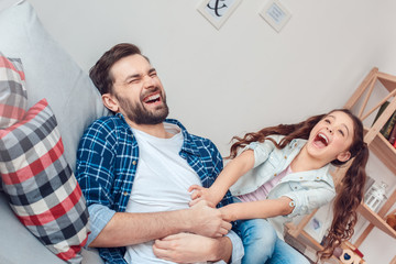 Father and little daughter at home lying girl tickling father screaming excited