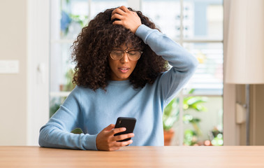 Beautiful african american woman using smartphone stressed with hand on head, shocked with shame and surprise face, angry and frustrated. Fear and upset for mistake.