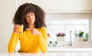 African american woman drinking orange juice in a glass very happy pointing with hand and finger