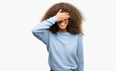 African american woman wearing a sweater smiling and laughing with hand on face covering eyes for...