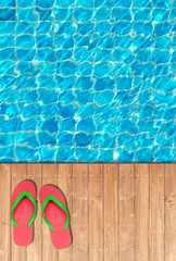 Wooden floor edge of swimming pool with red flip flops