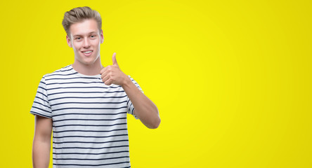 Young handsome blond man wearing stripes sailor t-shirt happy with big smile doing ok sign, thumb up with fingers, excellent sign