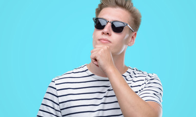 Fototapeta premium Young handsome blond man wearing sunglasess serious face thinking about question, very confused idea