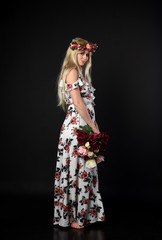 full length portrait of blonde girl wearing floral dress and a flower crown. standing pose against a black studio background.