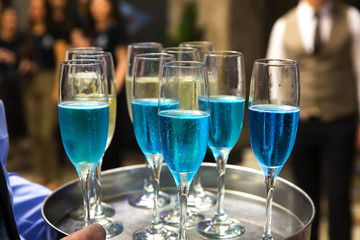The waiters greet guests with alcoholic drinks. Champagne, blue wine, white wine on trays.