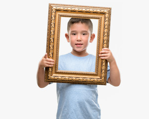 Dark haired little child holding frame pointing with finger to the camera and to you, hand sign, positive and confident gesture from the front