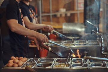 Cooking process in an Asian restaurant. Cook is stirring vegetables in wok.