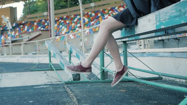 the legs of a woman are hanging at the football stadium. feet in red sneakers
