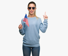 Beautiful young woman holding USA flag surprised with an idea or question pointing finger with...