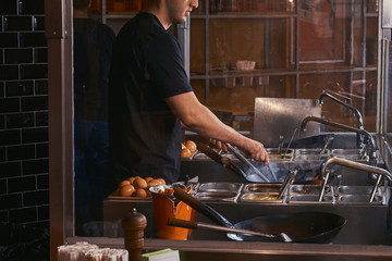 Cooking process in an Asian restaurant. Cook is stirring vegetables in wok.