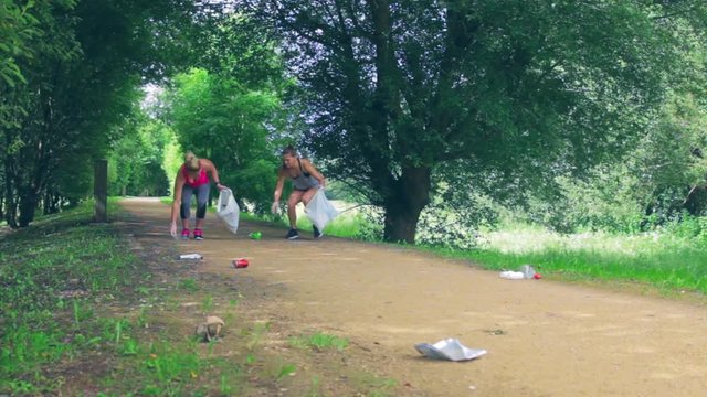 Waste pile and two girls running with bags doing plogging outdoors