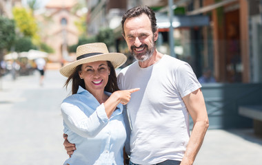 Obraz premium Middle age couple down the street very happy pointing with hand and finger