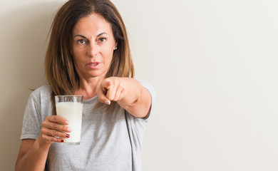 Middle age woman drinking a glass of fresh milk pointing with finger to the camera and to you, hand sign, positive and confident gesture from the front