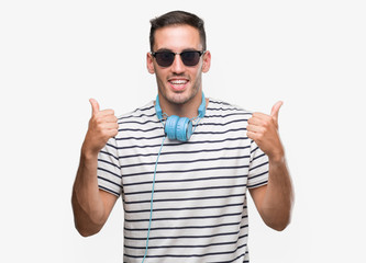 Naklejka premium Handsome young man wearing headphones success sign doing positive gesture with hand, thumbs up smiling and happy. Looking at the camera with cheerful expression, winner gesture.