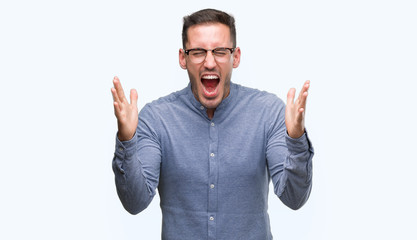 Handsome young elegant man wearing glasses celebrating mad and crazy for success with arms raised and closed eyes screaming excited. Winner concept