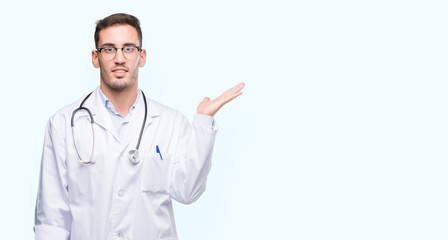 Handsome young doctor man smiling cheerful presenting and pointing with palm of hand looking at the camera.