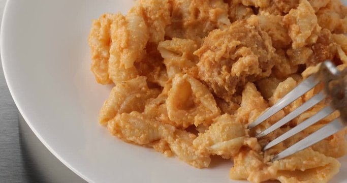 Close video of spicy chicken nuggets with macaroni and cheese on a white plate being eaten with a fork.