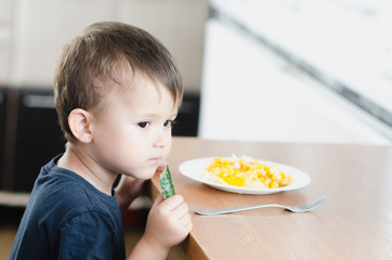 the child in the kitchen eating fresh cucumber and omelet