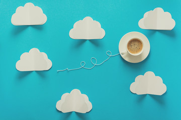 Coffee cup in shape of balloon with clouds on blue paper background. Toned
