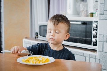the child greedily in the kitchen eating an omelet in the afternoon in the summer