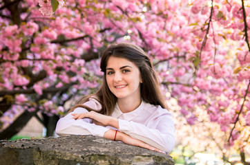 portrait of a young teenage girl looking at blooming sakura trees