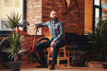 Handsome bearded hipster male in a blue fleece shirt and jeans sitting on a wooden stool at a...