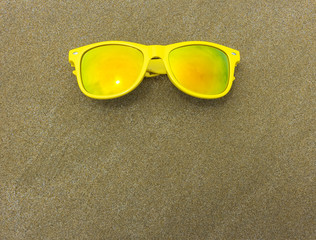 Top view of sunglasses on the beach near the blue sea with sand. Background with copy space.