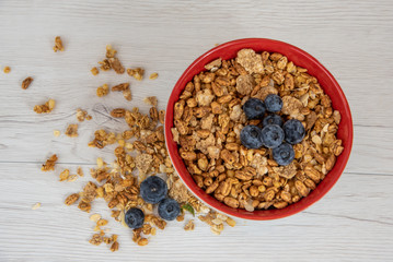 A red bowl on full of granola with berries on white wood table, top view
