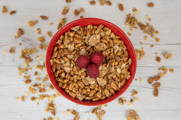 A red bowl on full of granola with berries on white wood table, top view
