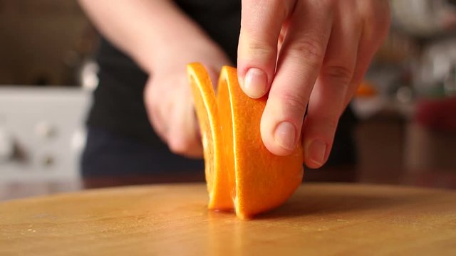 Hand slicing orange on wooden board. Woman young housewife in kitchen at home slicing fresh orange fruits on cutting board for salad or juicing. Healthy eating, cooking, dieting and people concept.