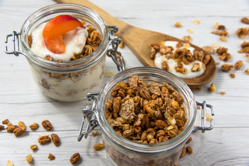 A jar fiiled with granola,wooden spoon whit granola, on white wood table, close-up,selective focus