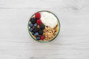 Bowl of cereals with yogurt and fresh berries on white wooden background from top view