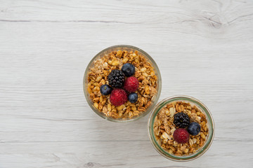 Two jars full of granola  whit berries on the white wood table, top view